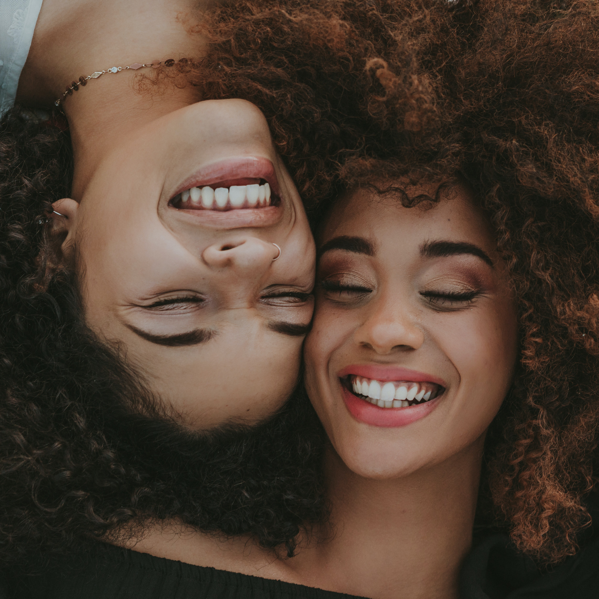 PCOS support: two women lying with heads next to one another laughing