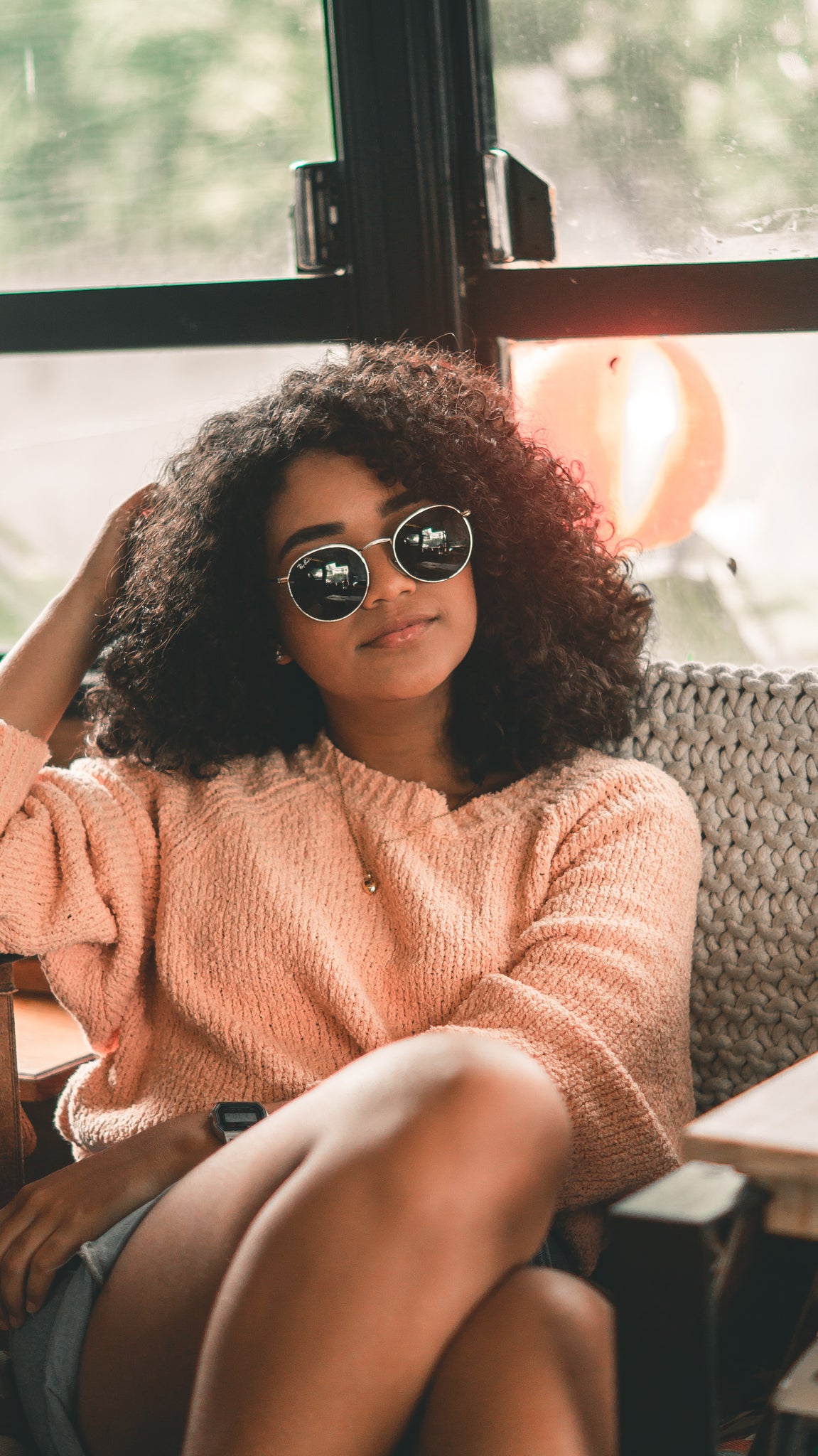 Woman wearing pink jumper and sunglasses sitting looking thoughtful