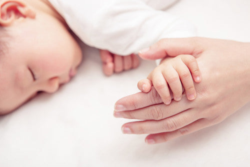 Sleeping baby holding mothers hand