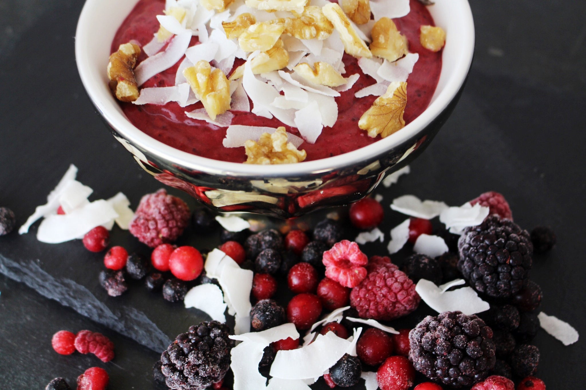 Triple berry smoothie in a bowl surrounded by fruit